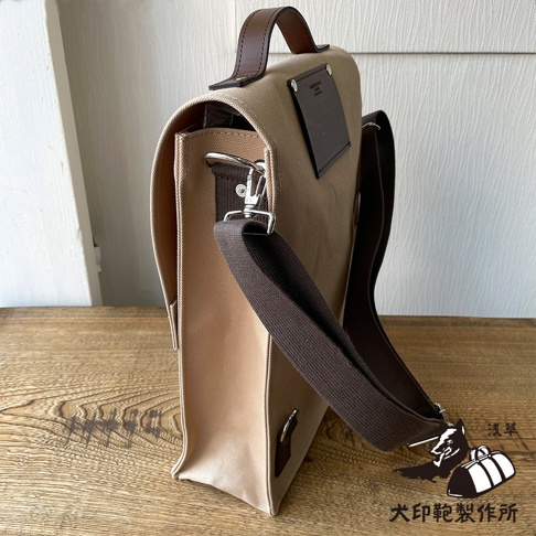 犬印純綿帆布三用直式側背包，米白色帆布主體搭配棕色皮革提把與肩帶，側面有金屬掛鉤與調節環，包蓋上有品牌壓印皮標。