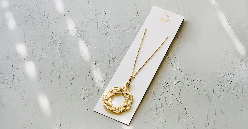 和風水引花結金絲項鍊，以金色細緻的鍊子搭配白色與金色的水引編織而成的花結吊墜，呈現典雅的日式風格。