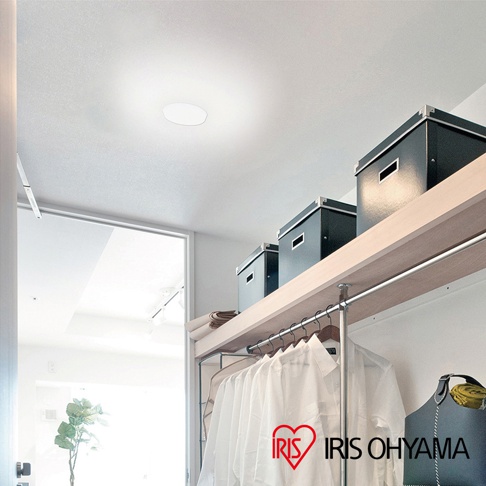 天花板上安裝了一個圓形白色LED小型吸頂燈，燈光柔和。下方是木質層架，層架上擺放著三個黑色收納盒，層架下方掛著一排白色衣物。