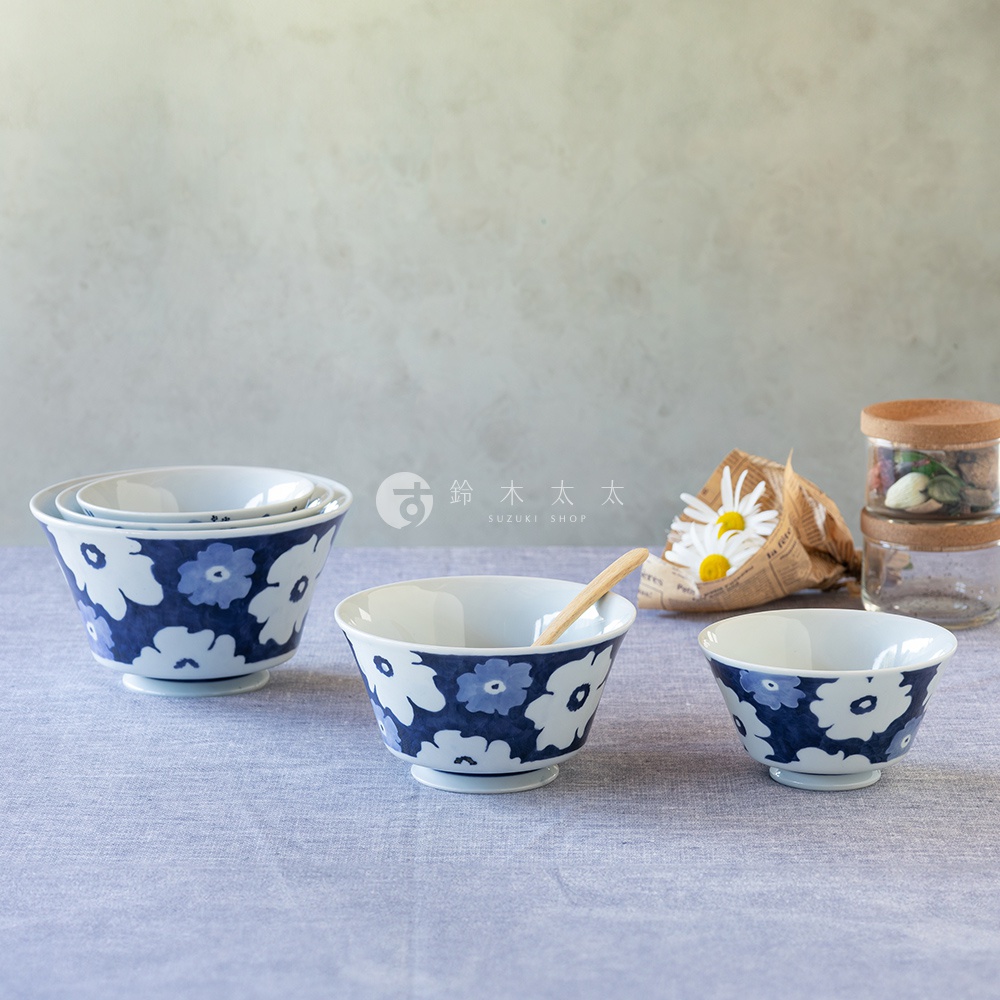 三個白色陶瓷丼飯碗，帶有藍色花卉圖案，擺放在藍色桌布上，其中一個碗內有一支木勺。