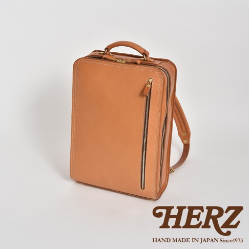 淺棕色皮革製成、結構方正的電腦後背包，配有兩個可調節的皮革肩帶，一個頂部提把，以及側邊和前方有拉鍊口袋。