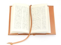 職人手作皮革附繩書套，顏色為自然棕色。書套由皮革製成，設計簡約，包含一本展開的書本，書本內頁為白色，印有黑色文字。一條皮革繩從書本中延伸出來，末端打結。