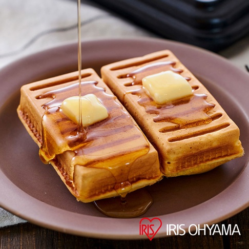 兩塊烤至金黃的熱壓三明治，上面各放著一塊融化的奶油，淋上琥珀色的糖漿，擺放在褐色的盤子上。