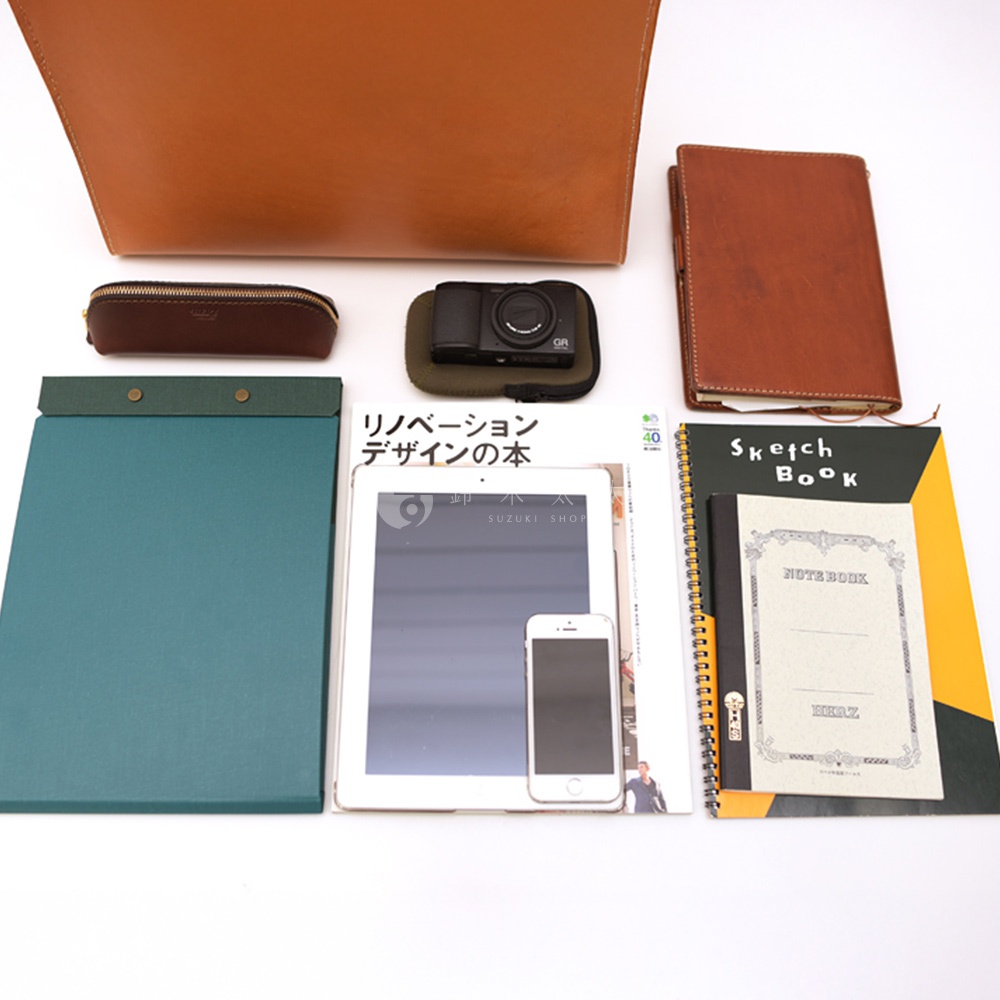 一組用於工作和藝術創作的物品，包括一個棕色的皮革公事包、一個皮製筆袋、一台相機、一本筆記本、一個平板電腦、一個手機、一個綠色的文件夾和一本筆記本，背景為白色。