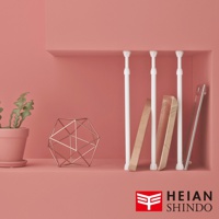 展示四根白色內建式彈簧伸縮桿，固定於粉紅色層架上，桿身為圓柱形，底部有白色圓形固定座。旁邊擺放著一盆綠色植物、一個銅色幾何裝飾物，以及兩塊木板和一片玻璃。