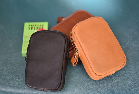 職人手作皮革菸盒收納包，包含深棕色與淺棕色兩款，皆為拉鍊開合設計，材質為皮革。