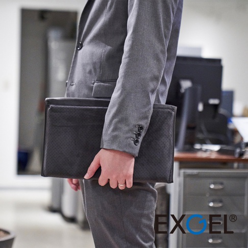 黑色皮革材質的行動折疊腰靠坐墊D，表面有細緻的透氣孔設計，由穿著灰色西裝的人士手持。