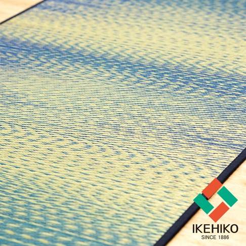 藺草榻榻米瑜珈墊，表面為淺黃色藺草編織，飾有藍色漸層的條紋圖案，邊緣包覆黑色滾邊。