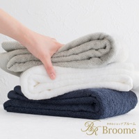 疊放的三條今治純棉長浴巾，分別為淺灰色、白色和海軍藍，手部觸碰頂部淺灰色浴巾，浴巾表面有細緻的菱紋織紋。