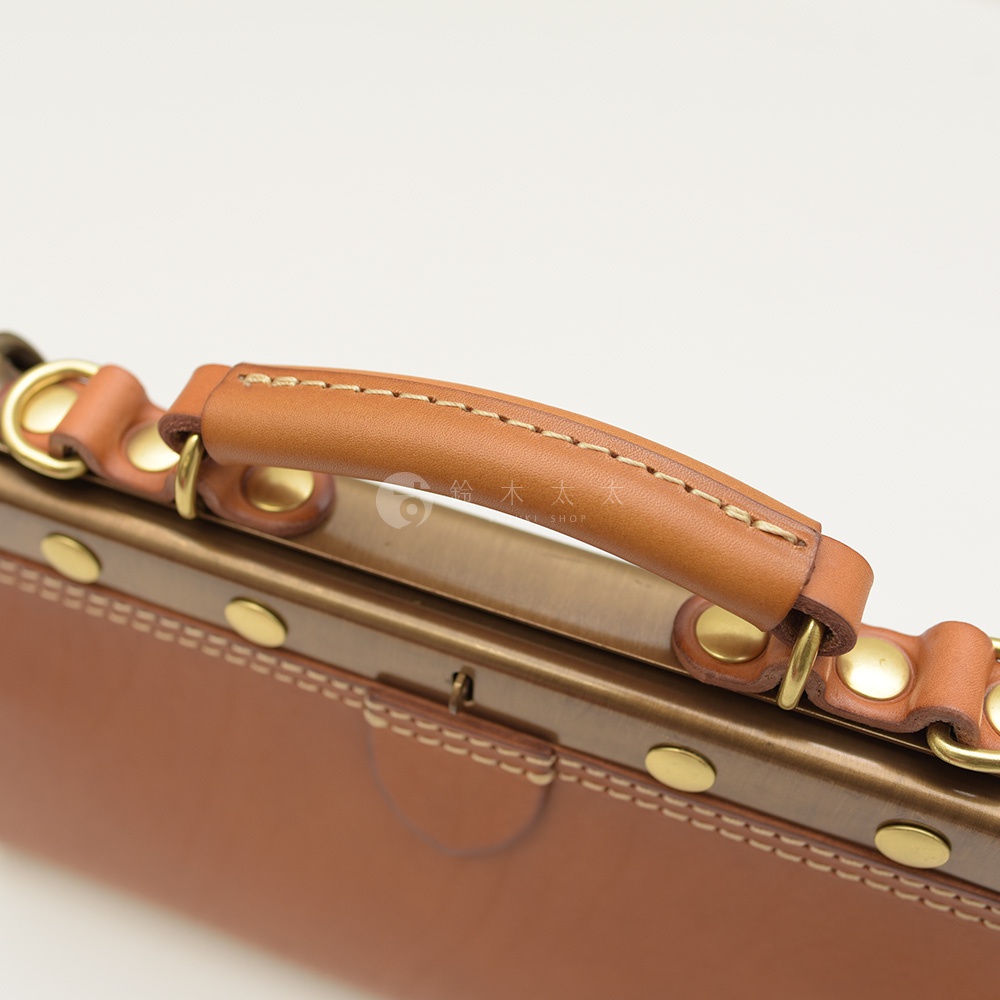 職人手作皮革復古口金兩用手提包 P-8，淺棕色皮革提把，搭配古銅色金屬框架與圓形铆釘，包身皮革顏色為棕色，縫線精緻。