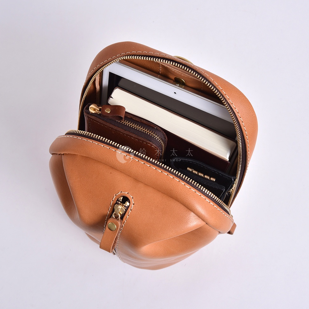 日本HERZ職人手作皮革立體運動斜背包，棕色光滑皮革材質，主收納空間拉鍊打開，可見平板電腦、書籍及皮夾等物品。