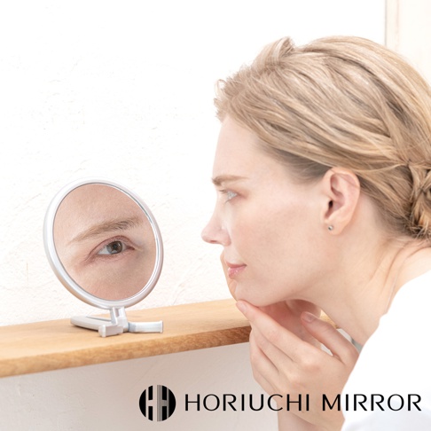 堀內鏡 HORIUCHI MIRROR 的 Napure 手持立式兩用3倍美妝鏡，一位女子正對著鏡子檢視臉部細節