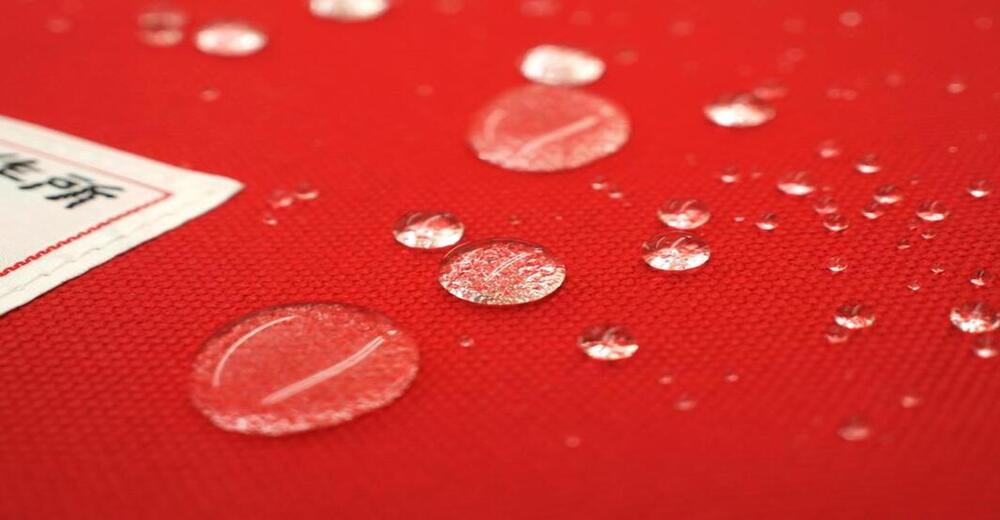 紅色純棉帆布材質的收納包表面有許多水珠，左上角有一個白色標籤。