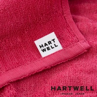 近拍的粉紅色毛巾，織紋清晰可見，上面縫有一個白色標籤，印有黑色字樣 HART WELL。