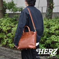 職人手作棕色皮革大容量兩用托特包，附有可拆卸肩帶，包款底部有四個金屬腳釘，整體呈現復古風格。