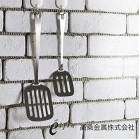 兩個日製不鏽鋼輕薄煎匙，銀色，帶有長柄和帶有長條形孔洞的鍋鏟頭，懸掛在白色磚牆上。