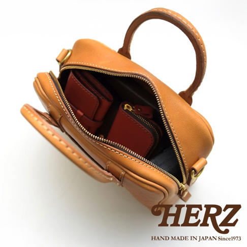 HERZ 職人手作皮革兩用迷你波士頓包，可見內部裝有紅色皮夾和拉鍊零錢包，包款為棕褐色牛皮材質，以精緻車縫線工藝製作。
