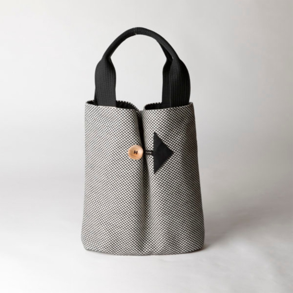 三河木綿刺子織直式收納托特包，採用黑白格紋布料，配有黑色提把，正面有一個黑色箭頭形狀裝飾，中央有木質鈕扣。