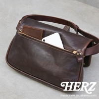 職人手作皮革斜背包，深棕色，有拉鍊主袋和外袋，展示手機和卡夾，皮革質感。