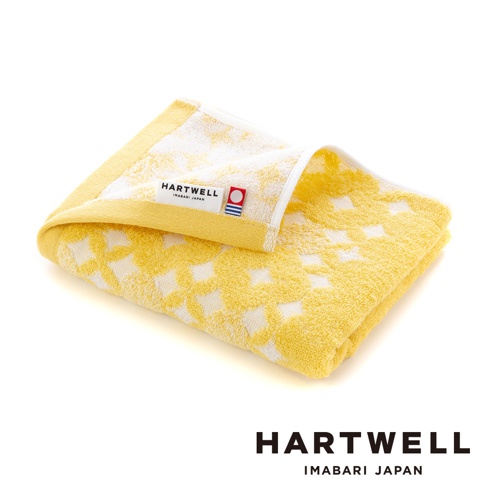 一條黃色與白色交織的毛巾，帶有傳統的幾何紋樣，材質為棉，標籤上有「HARTWELL IMABARI JAPAN」字樣。