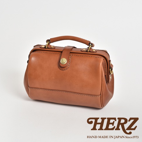 一個棕褐色的皮革醫生包，採用復古口金設計，配有頂部提把和可拆卸肩帶。包身線條簡潔，縫線工整，金色金屬配件增添質感。