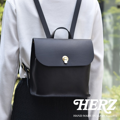 黑色皮革翻蓋迷你後背包，配有金色旋轉鎖扣和可調節肩帶，簡約設計，適合日常攜帶。