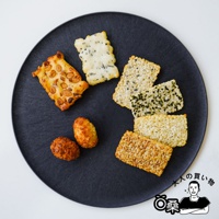 黑盤上擺放著多種米菓，包含花生米菓、點綴海苔的米菓、以及原味和焦糖色米菓，還有兩顆金黃色的炸米球。