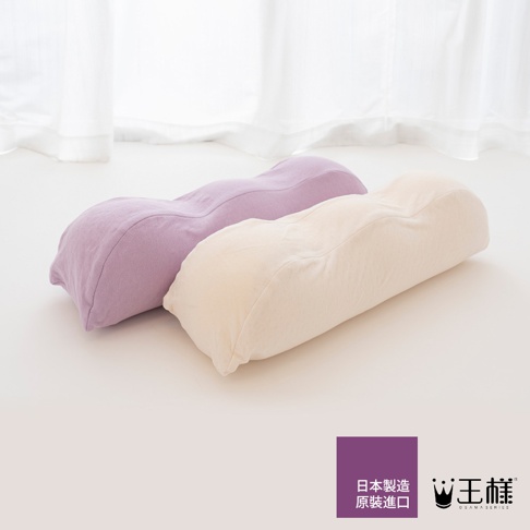 兩個女人の美容抬腿枕，一個為淡紫色，另一個為淺米色，皆為曲線造型，布料材質，放在白色平面上，背景為淺色窗簾。