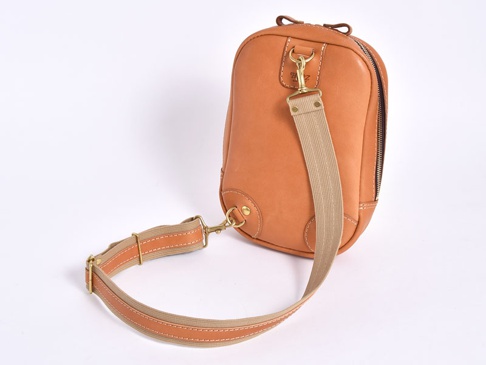 職人手作皮革立體運動斜背包，採用天然棕色皮革，搭配米色織帶和金屬扣環，設計簡潔實用。