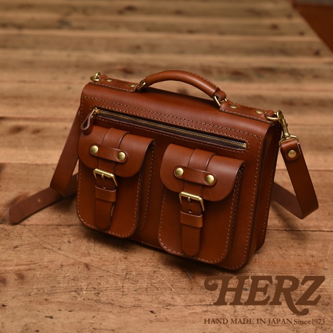 職人手作棕色皮革雙口袋兩用單肩包，配有金屬釦環和拉鍊，可肩背或手提。
