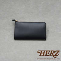 黑色皮革製的拉鍊長夾，上方有金色拉鍊，右下角有HERZ字樣和HAND MADE IN JAPAN Since1973字樣。