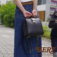 黑色皮革迷你後背醫生包，採用經典醫生包造型，配有金色旋轉鎖扣及裝飾性卯釘，皮革材質光滑有質感，展現職人手作的精緻工藝。