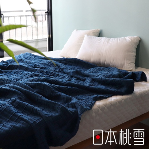 深藍色八層紗雙人被鋪在白色床鋪上，被子表面有立體紋理，旁邊擺放著兩個白色枕頭。