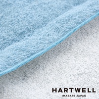 淺藍色與白色毛巾布料特寫，展示細緻柔軟的毛圈質地，以及藍色滾邊縫線，品牌標誌 HARTWELL IMABARI JAPAN 位於右下方。