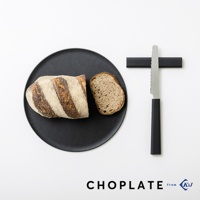 一個黑色圓形砧板盤上放著切開的麵包，旁邊有一個帶有黑色手柄的銀色鋸齒刀，刀身靠在黑色支架上。