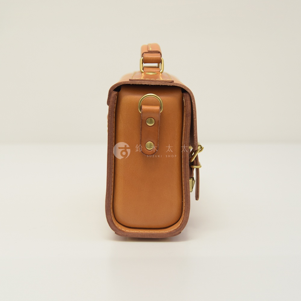 棕色皮革製成的手提包，設有可拆卸肩帶，包身側面有 D 型環和金屬扣，風格簡約。