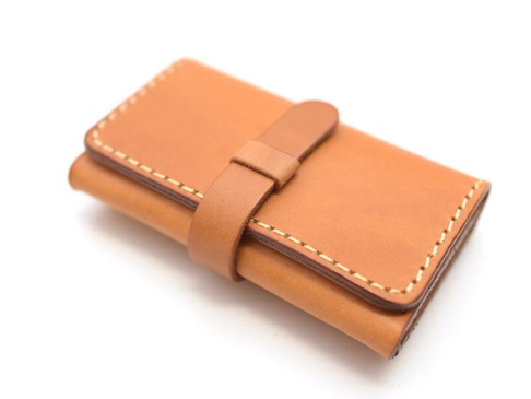 一個淺棕色皮革名片收納夾，採用壓扣式設計，邊緣有縫線裝飾，整體為簡約經典風格。