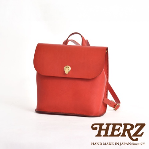 紅色皮革翻蓋迷你後背包，帶有金色旋轉鎖扣和可調式背帶，展現職人手作質感。