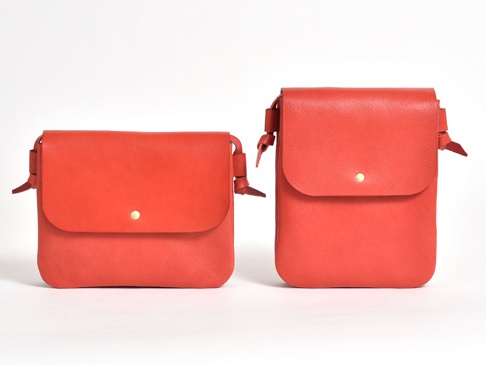 兩個紅色皮革隨行袋，一個橫式較寬，一個直式較高，均有金色按扣和綁結裝飾。