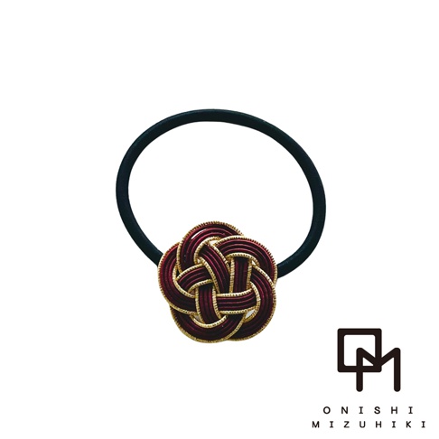 一款深紅色和金色線材編織而成的日式水引花結髮圈，搭配黑色彈性髮圈。