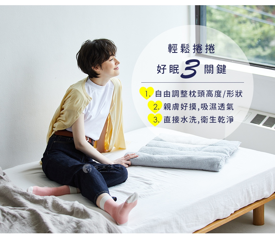 一名女子坐在床上，身上穿著白色T恤、黃色開襟外套和深藍色長褲，旁邊有一個捲起來的灰色毛巾枕。