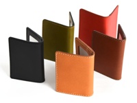 五款職人手作皮革雙折票券收納夾，顏色包含黑色、橄欖綠、橘色、紅棕色及紅色。皆為皮革材質，縫線清晰。