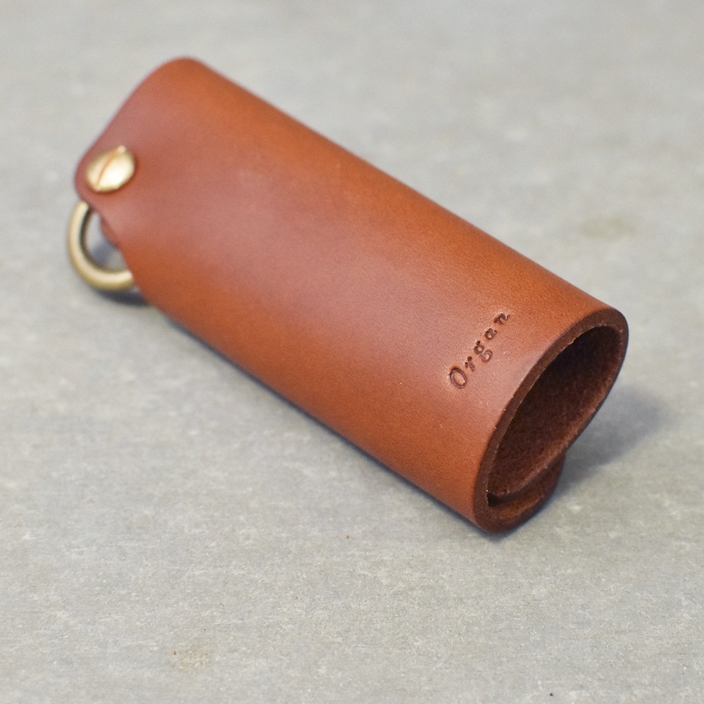 棕褐色皮革製成的圓筒狀鑰匙套，頂部有黃銅扣環和鑰匙圈，側面壓印有「Organ」字樣。