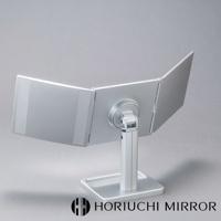 銀色金屬材質的桌上型三折化妝鏡，鏡面可360度旋轉調整，左側鏡面有碳纖維紋理裝飾，置於方形底座上。