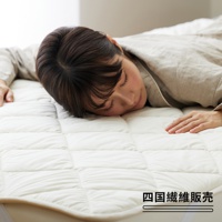 一張雙人加大尺寸的米白色羊毛床墊，表面有規則的絎縫格紋，一位女子正舒適地趴臥在床墊上。