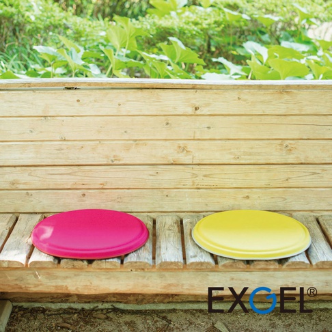 MARU PUNI 圓座墊：鮮豔桃紅色和亮黃色圓形座墊，柔軟材質，放置於木質長椅上，背景為綠色植被。