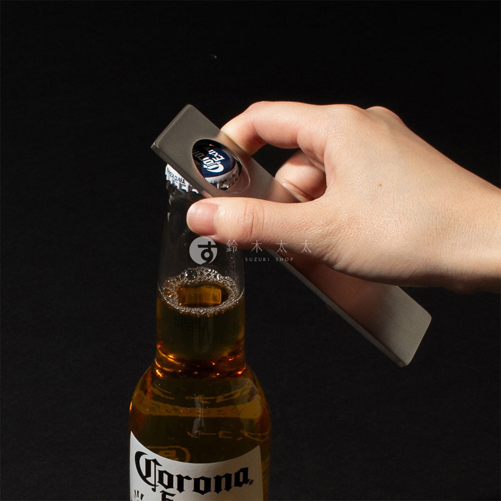 一只手正使用銀色不鏽鋼開瓶器開啟一瓶啤酒。
