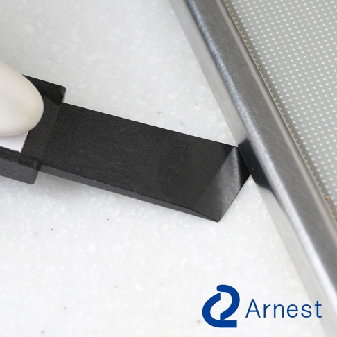 黑色塑膠刮刀的尖端緊貼不銹鋼邊緣，刮刀與淺灰色帶有圓點圖案的表面接觸。