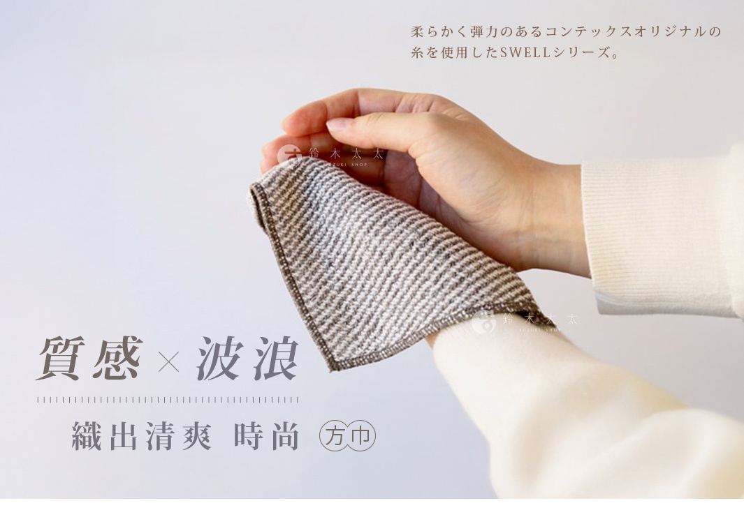 一塊淺棕色與米白色交織的波浪紋方巾，材質看起來柔軟，由細緻的紗線織成，一隻手正拿著這塊方巾，另一隻手腕穿著白色長袖衣物。