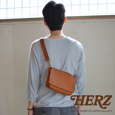 一個穿著灰色上衣的人斜背著棕色皮革包，包包的款式簡約，皮革材質看起來質感良好。